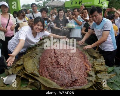 Les citoyens partagent un énorme zongzi, une boulette en forme de pyramide fait de riz gluant enveloppé dans des feuilles de roseau ou de bambou dans la ville de Liuzhou, Guangxi en Chine du sud Banque D'Images