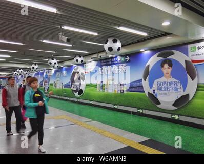 --FILE--passagers à pied passé une publicité de Mengniu Dairy pour la prochaine Coupe du Monde FIFA 2018 est vue à une station de métro de la ligne de métro de Beijing Banque D'Images