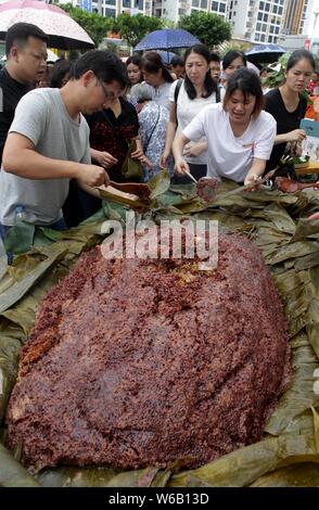 Les citoyens partagent un énorme zongzi, une boulette en forme de pyramide fait de riz gluant enveloppé dans des feuilles de roseau ou de bambou dans la ville de Liuzhou, Guangxi en Chine du sud Banque D'Images