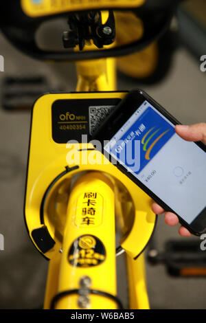 Un utilisateur de téléphone mobile met son smartphone au-dessus d'une location de vélos en libre-service chinois ofo avec NFC-activé smart lock pour le déverrouiller au campus de Banque D'Images