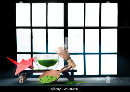 Thé vert matcha dans un bol à thé en verre double paroi avec un fouet en bambou et une grue origami rouge. Portes coulissantes Shoji traditionnel japonais,fond cere Banque D'Images
