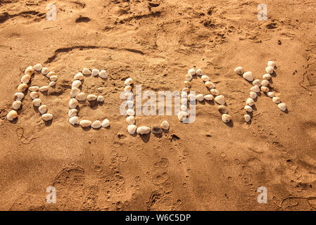 L'inscription 'RELAX', assemblés à partir de grandes coquilles blanc sur la mer de sable. Banque D'Images