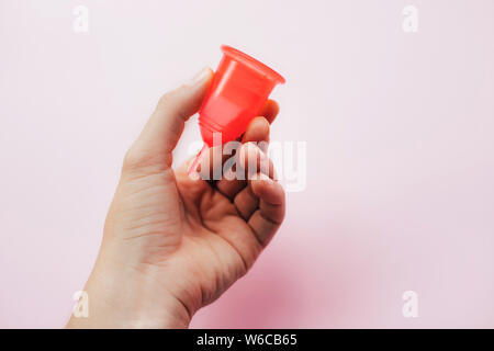 Woman's hand holding coupelle menstruelle sur fond rose. La santé de la femme et de produits d'hygiène féminine écologique concept. Banque D'Images