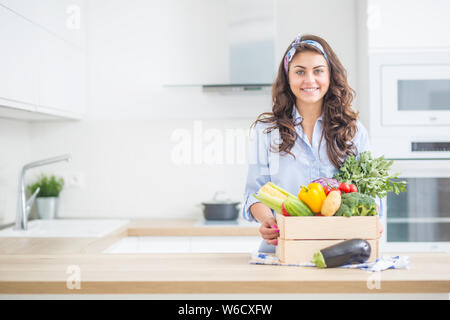 Femme dans sa cuisine avec boîte en bois plein de légumes de culture biologique. Banque D'Images