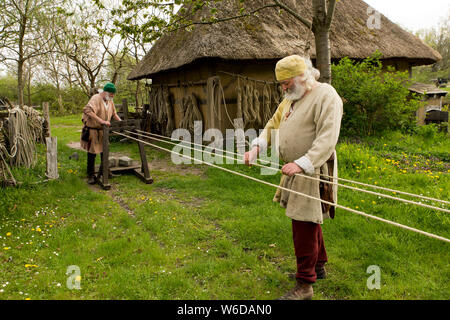 Deux hommes en tissu traditionnel du moyen age produire corde au centre médiéval de plein air à Nykøbing Falster, Danemark. Le centre médiéval est construit autour du village à Sundkøbing un fjord que c'était autour de l'année 1400. Les maisons sont conçues et construites de manière authentique avec les gens qui peuplent le village, hommes, femmes, enfants, paysans, artisans, guerriers et chevaliers etc s'habiller et de travailler comme ils le feraient de nouveau en 1400. Chanoines et grands trébuchets peut être vu tirer des missiles, des chevaliers en armures à cheval en concurrence avec des lances et des épées, les teinturiers textiles de coloration avec des plantes et de la con Banque D'Images