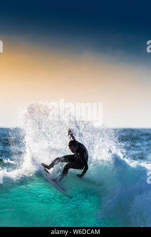 Un surfer une vague par le contre-jour coucher de soleil à Newquay dans Fistral à Cornwall. Banque D'Images