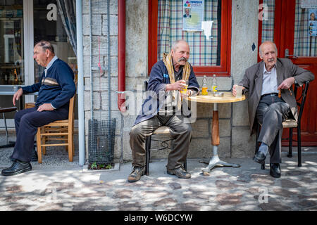 Trois personnes âgées hommes grecs s'asseoir à l'ombre d'un village cafe observant la scène qui passe et profiter d'une boisson Banque D'Images