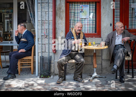 Trois personnes âgées hommes grecs s'asseoir à l'ombre d'un village cafe observant la scène qui passe et profiter d'une boisson Banque D'Images