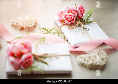 Quelques boîtes cadeau enveloppées de papier blanc artisanal simple et décorées avec un bouquet de roses et un bouquet de verts Banque D'Images