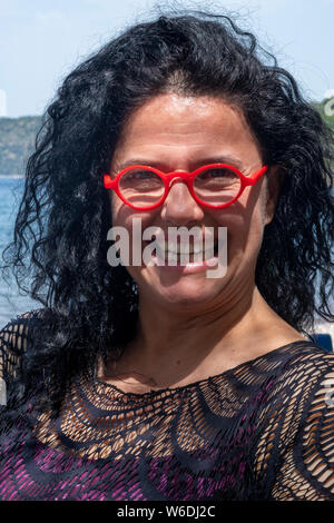 Jolie femme sur une plage en Grèce portant des lunettes rouge vif Banque D'Images