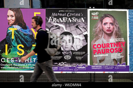 Un jeune homme marchant par affiches publicitaires pour Edinburgh Fringe Festival montre. Edinburgh, Ecosse, Royaume-Uni. (With motion blur) Banque D'Images