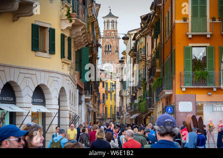 À Vérone, Italie, la foule des touristes à la mode, colorée rue piétonne Via Giuseppe Mazzini. Le 12ème tour des Lamberti dépasse. Banque D'Images