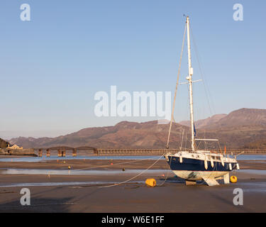 Barmouth, Gwynedd, Pays de Galles, Royaume-Uni : la marée basse dans l'estuaire de Mawddach a laissé un yacht baché dans le port. Cadair Idris est en arrière-plan. Banque D'Images