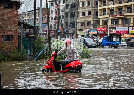 Srinagar, Inde. 06Th Aug 2019. Un homme pousse son scooter à travers un chemin d'eau- connecté après les fortes pluies de Srinagar.pluies diluviennes ont causé l'engorgement dans de nombreux domaines de Srinagar exposant le mauvais drainage de la ville. Le temps le ministère a prévu de fortes pluies pour les prochains jours l'ensemble de la région. Credit : SOPA/Alamy Images Limited Live News Banque D'Images