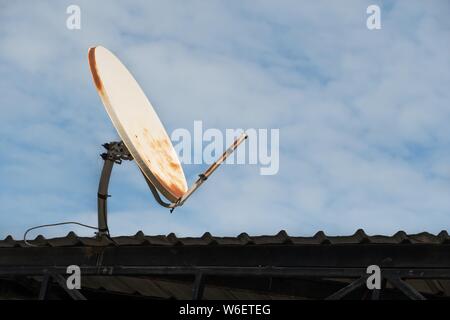 Brisée et vieille antenne satellite sur le toit et fond de ciel bleu. Banque D'Images