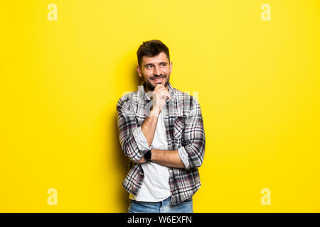 Close up portrait of man qui a l'air loin de toucher son menton et pèse les avantages et inconvénients de l'offre isolé sur un jaune vif backgrou Banque D'Images