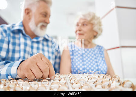 Homme barbu avec des cheveux gris à carreaux chemise bleu portant le choix de bague en or pour sa belle femme élégante dans une bijouterie. Faire de la Joie aux êtres chers concept Banque D'Images