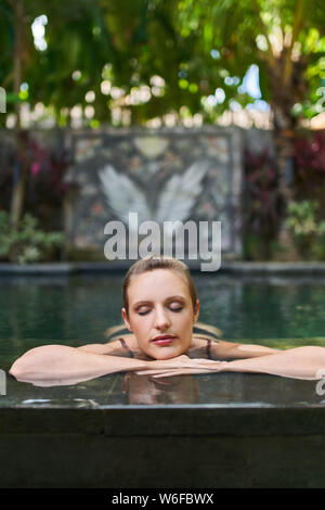 Belle femme zen détente en plein air dans une luxuriante et pierre moderne piscine d'hôtel de luxe lors de voyages tropicaux à Bali Banque D'Images