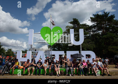 Kostrzyn Nad Odra, Pologne. 06Th Aug 2019. Les visiteurs s'assoient sur le Pol'et'Rock Festival en face d'un grand lettrage ('I Love U Hater') dans le soleil. Le festival gratuit pour les visiteurs aura lieu du 01.08.2019 pour la 25e fois, jusqu'à 03.08.2019 à Kostrzyn nad Odra. Credit : Gregor Fischer/dpa/Alamy Live News Banque D'Images