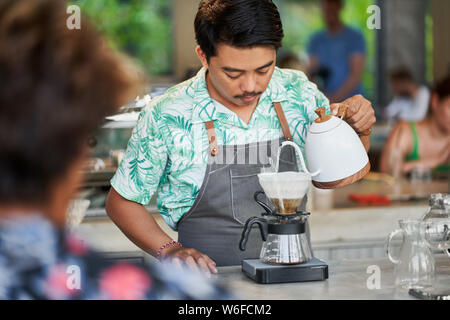 Vie candide shot of indonesian ethniques barista et propriétaire de petite entreprise la préparation du café bio-équitable dans un café branché Banque D'Images