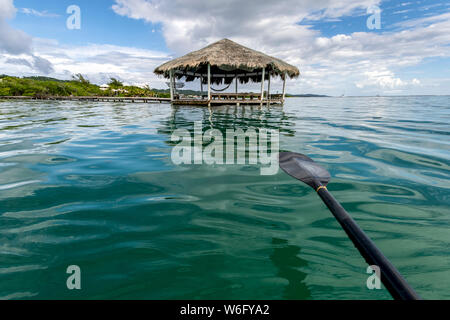 Un bateau pagayez sur l'eau turquoise avec un abri à l'extrémité du quai et la côte d'une île des Caraïbes; Honduras Banque D'Images