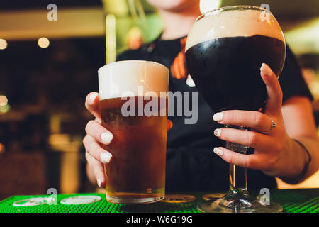 Barman verse la bière sombre dans un verre au bar de près. Banque D'Images