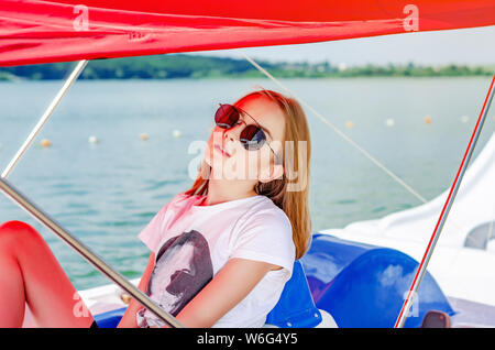 Jeune fille blonde à lunettes, portrait sur sous un auvent rouge sur le fond du lac. Banque D'Images