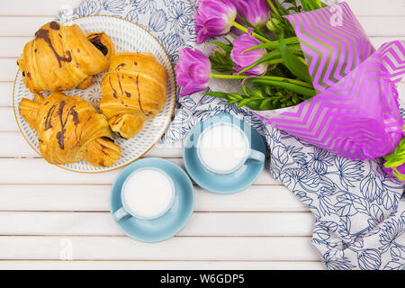 Trois croissants, deux tasses de café sur la table et un bouquet de belles tulipes. Banque D'Images