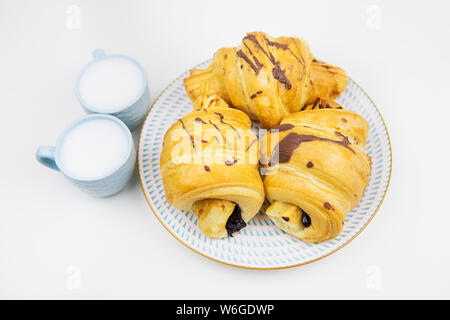 Trois croissants fraîchement cuits sur une plaque en céramique blanche, deux tasses de café. Banque D'Images