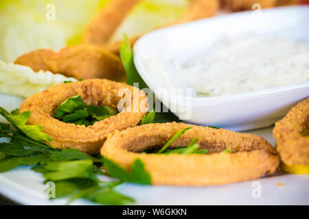 Anneaux de calmars savoureux dans la farine à pain. Squid est servi avec sauce verts et verts frais avec des tomates et de la laitue. Banque D'Images