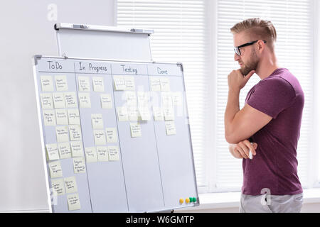 Un jeune businessman standing in Office Looking at notes adhésives sur tableau blanc Banque D'Images