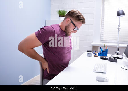 Vue latérale d'un jeune homme assis sur une chaise de bureau à avoir mal au dos Banque D'Images
