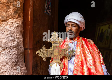 Prêtre tenant une croix processionnelle élaborée sur la tombe d'Adam dans le groupe Nord de la Rock-Hewn églises ; Lalibela, région d'Amhara, en Éthiopie Banque D'Images