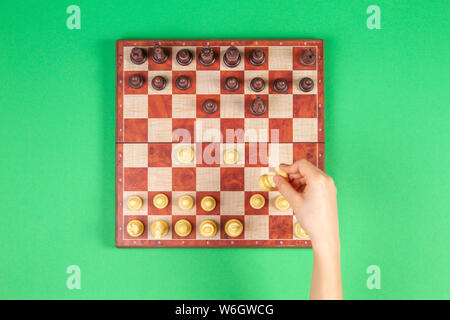 Kid mains sur un échiquier jouant aux échecs sur fond vert, vue du dessus Banque D'Images