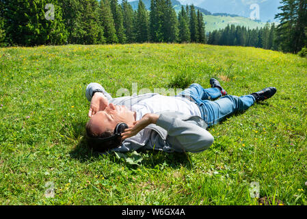 Man Relaxing Lying in Field d'herbe à l'écoute de la musique dans les montagnes Banque D'Images