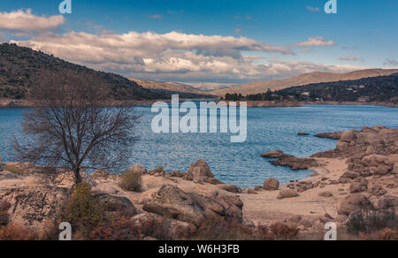 Tiemblo, Avila, Castille et Leon, Espagne - 24 novembre 2013 : vue d'un coucher de soleil sur un lac d'eau bleue, avec un arbre à l'avant et un montagnes enneigées en th Banque D'Images