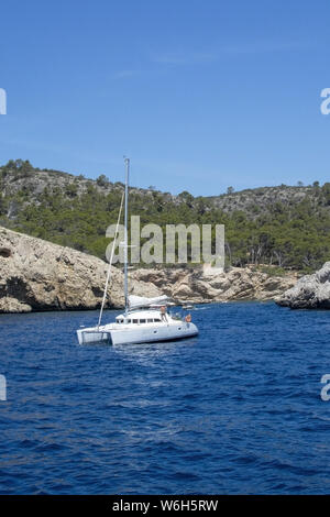 MALLORCA, ESPAGNE - Juin 23, 2019 : White camaran avec les gens l'ancre près de la côte rocheuse sur une journée ensoleillée le 23 juin 2019 à Mallorca, Espagne. Banque D'Images