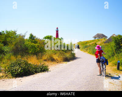 Retour Voir les cyclistes voyageant sur la route en direction de phare dans Schiermonnikoog, sur dune de sable sur fond de ciel bleu. La Hollande. Pays-bas Banque D'Images