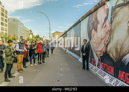 BERLIN, ALLEMAGNE - 26 septembre 2018 : asian man de prendre une photo sur le trottoir près de la "Le baiser de la mort" de peindre sur le mur de Berlin à Banque D'Images