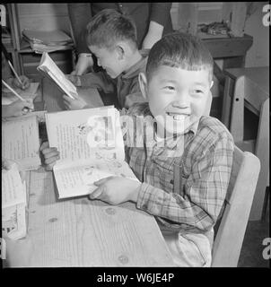 Manzanar Manzanar, Centre de réinstallation, en Californie. Une élève de la troisième année est enseigné à lire et . . . ; Portée et contenu : la légende complète pour cette photographie se lit comme suit : Manzanar Manzanar, Centre de réinstallation, en Californie. Une élève de la troisième année est enseigné à lire et à apprécier des livres pour enfants, comme tout autre jeune garçon américain. Cette photo a été prise par l'étudiant dans un centre de formation, où les enseignants reçoivent des crédits universitaires pour leur travail ici. Tous les cours sont supervisés par des enseignants accrédités. Banque D'Images