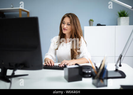 Happy Young Woman's Hand Typing On Computer Keyboard In Office Banque D'Images