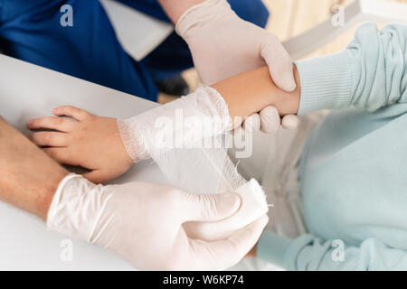 Médecin en uniforme bleu faire bandée élastique autour d'un garçon part avec traumatisme dans son bras. Banque D'Images