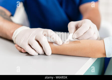 Patch médical. Médecin en uniforme bleu faire bandée élastique autour d'un garçon part avec son bras en traumatologie à l'hôpital. Banque D'Images