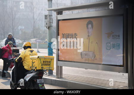 --FILE--un livreur de l'entreprise de livraison de nourriture en ligne chinois Meituan rides passé une publicité pour Meituan à Beijing, Chine, 27 décembre 2017. C Banque D'Images