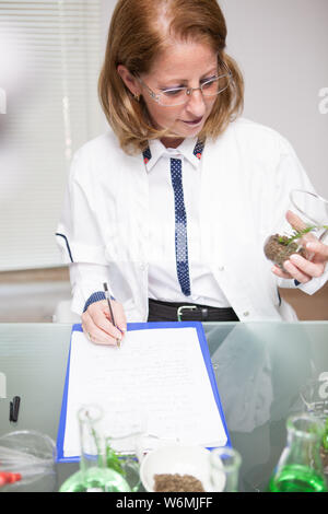 Femme d'âge moyen des notes après les essais microbiologiques sur le sol. Biologiste travaillant dans un laboratoire de recherche. Banque D'Images