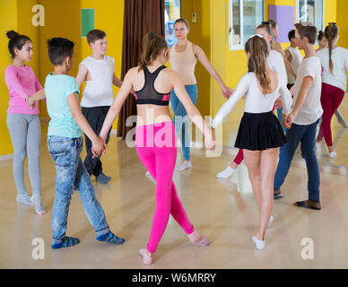 Groupe d'enfants avec leur enseignant, se tenant la main et la danse de l'école de danse en cercle Banque D'Images
