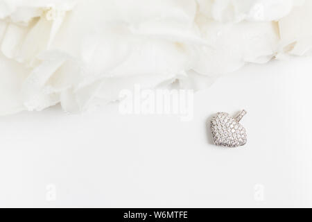 Pendentif en or blanc de forme de coeur avec des diamants et bouquet de roses blanches avec l'exemplaire de l'espace. Mise à plat. Vue d'en haut. Immersive. Beaux bijoux pour valent Banque D'Images