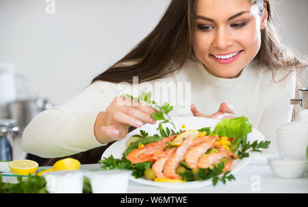 Smiling brunette girl decorating du poisson frit avec des herbes sur la plaque Banque D'Images