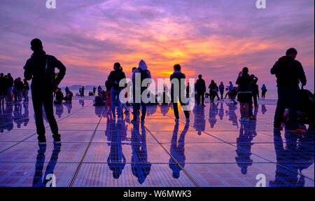 Silhouette de personnes contre un coucher de soleil orange et violet du monument du salut au soleil. Zadar, Croatie Banque D'Images