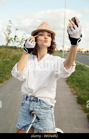 Fun brunette young woman cyclist applique les cosmétiques le road Banque D'Images